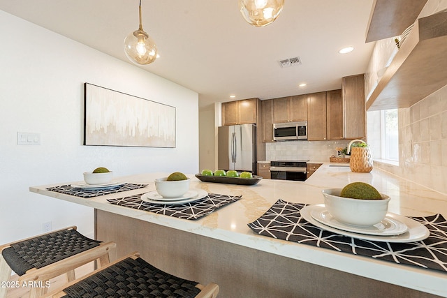 kitchen with appliances with stainless steel finishes, a breakfast bar, backsplash, hanging light fixtures, and kitchen peninsula