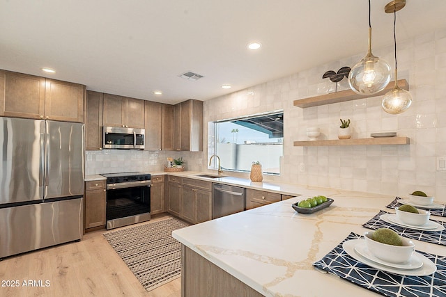 kitchen featuring sink, hanging light fixtures, stainless steel appliances, light stone countertops, and light wood-type flooring