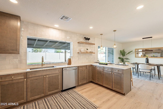 kitchen with decorative light fixtures, dishwasher, sink, kitchen peninsula, and light wood-type flooring