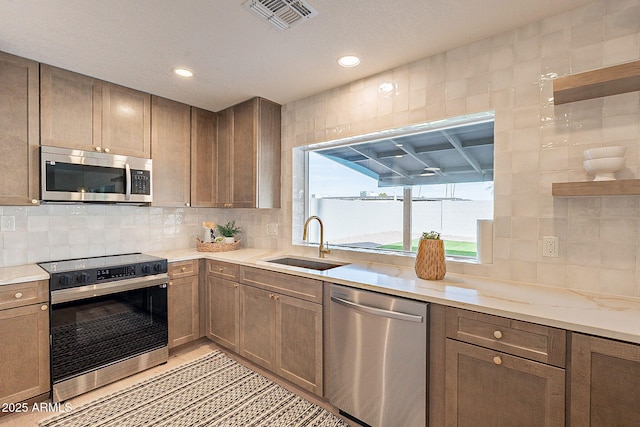 kitchen with light stone counters, sink, backsplash, and stainless steel appliances