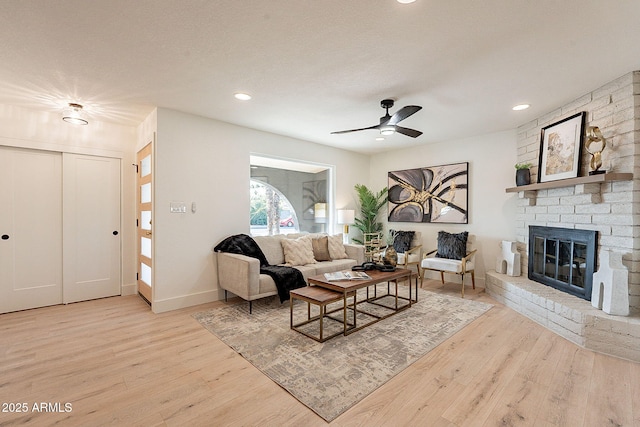 living room featuring a fireplace, a textured ceiling, light hardwood / wood-style flooring, and ceiling fan