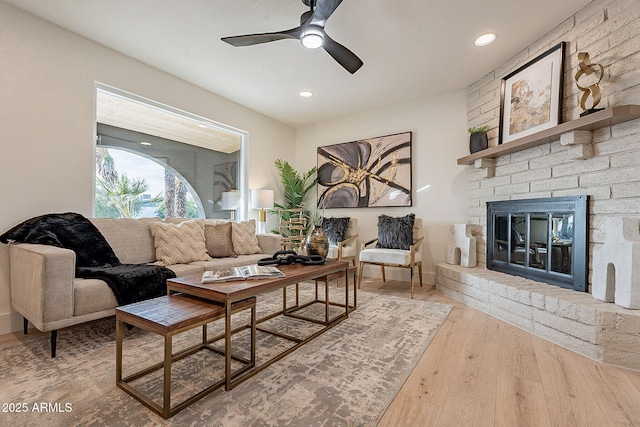 living room with wood-type flooring, a brick fireplace, and ceiling fan