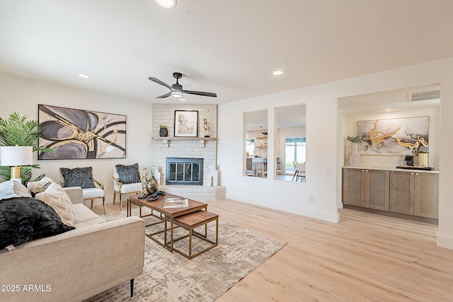 living room with a brick fireplace, ceiling fan, and light wood-type flooring