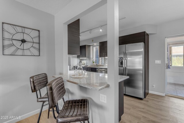 kitchen featuring light wood-style flooring, modern cabinets, appliances with stainless steel finishes, a kitchen breakfast bar, and light stone counters