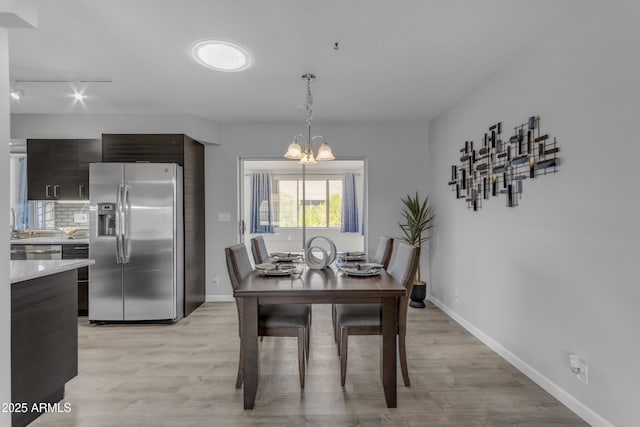 dining space featuring light wood-style floors, baseboards, and an inviting chandelier