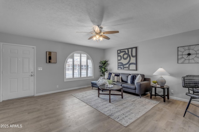 living room with a textured ceiling, ceiling fan, light wood-type flooring, and baseboards