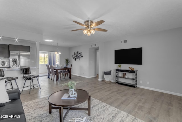 living area with light wood-style flooring, visible vents, baseboards, and ceiling fan with notable chandelier