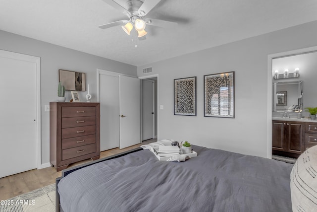 bedroom featuring ceiling fan, a sink, visible vents, light wood-type flooring, and ensuite bath