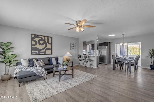 living room featuring light wood-type flooring, baseboards, and ceiling fan with notable chandelier