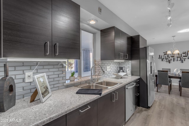 kitchen featuring light stone counters, dark brown cabinetry, a sink, appliances with stainless steel finishes, and light wood finished floors