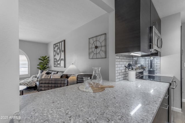 kitchen with light stone counters, open floor plan, a peninsula, stainless steel appliances, and dark cabinetry