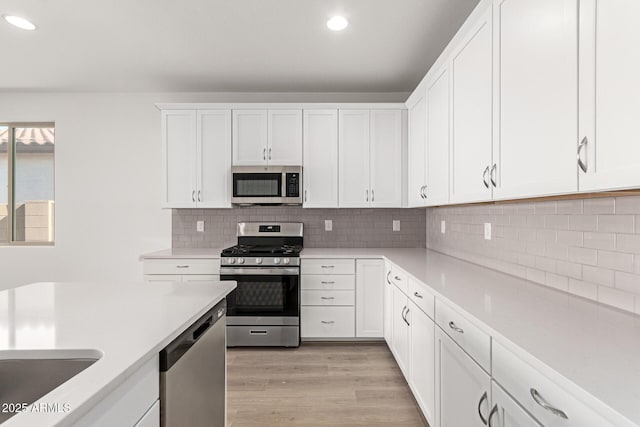 kitchen with light hardwood / wood-style floors, white cabinets, tasteful backsplash, and appliances with stainless steel finishes