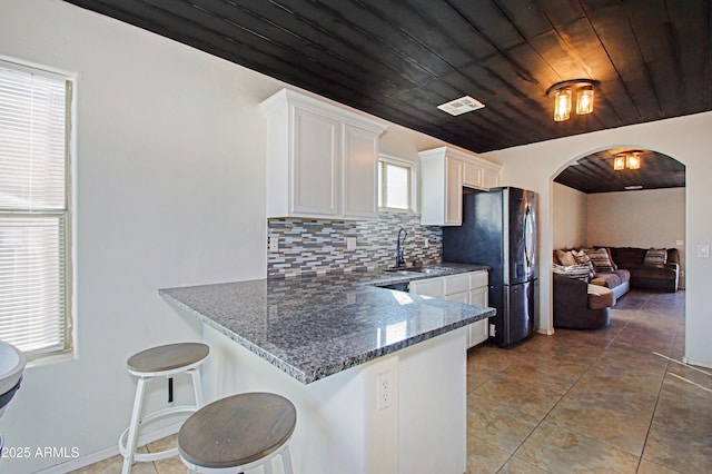 kitchen with white cabinetry, a breakfast bar, stainless steel fridge, and wood ceiling