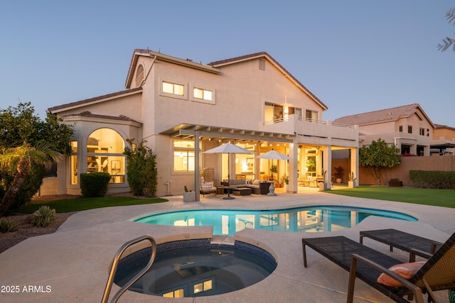 back house at dusk with a lawn, a patio, a pool with hot tub, an outdoor hangout area, and a balcony