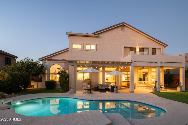 back house at dusk featuring a balcony, an outdoor hangout area, and a patio area