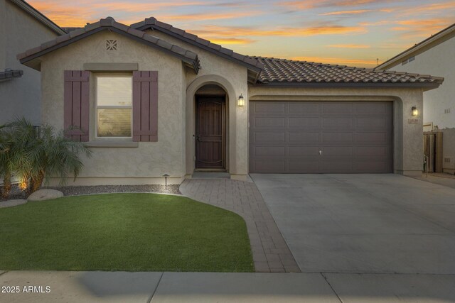 mediterranean / spanish home with an attached garage, a tiled roof, concrete driveway, and stucco siding