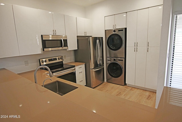 kitchen with stacked washer and clothes dryer, a sink, stainless steel appliances, white cabinets, and light wood finished floors