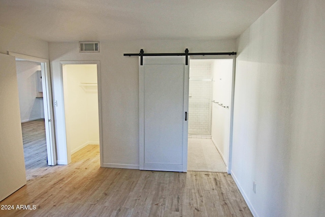 unfurnished bedroom featuring ensuite bathroom, a barn door, light hardwood / wood-style floors, a spacious closet, and a closet