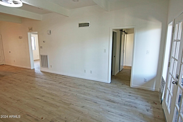 spare room with light hardwood / wood-style floors, a barn door, and beamed ceiling