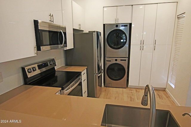 kitchen featuring stacked washer and dryer, stainless steel appliances, white cabinets, light hardwood / wood-style flooring, and sink