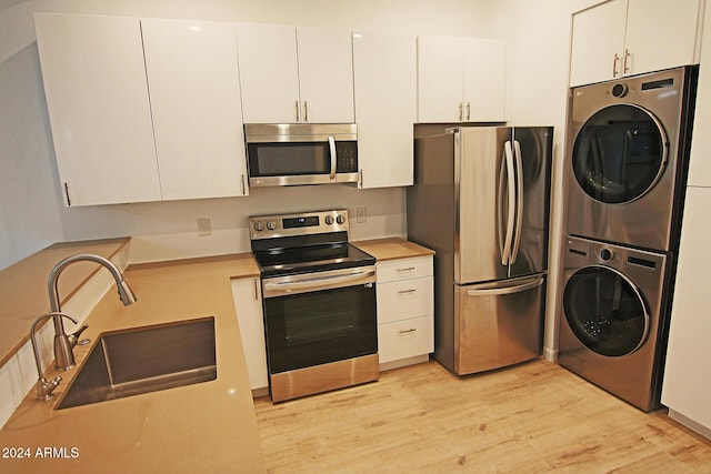 kitchen with appliances with stainless steel finishes, stacked washer / dryer, white cabinets, light hardwood / wood-style flooring, and sink