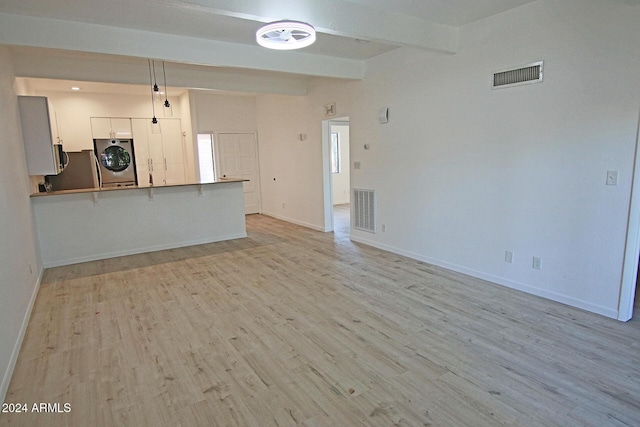 unfurnished living room featuring beam ceiling, washer / clothes dryer, and light hardwood / wood-style flooring