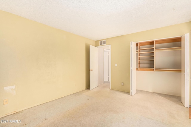 unfurnished bedroom featuring a textured ceiling, light colored carpet, and a closet