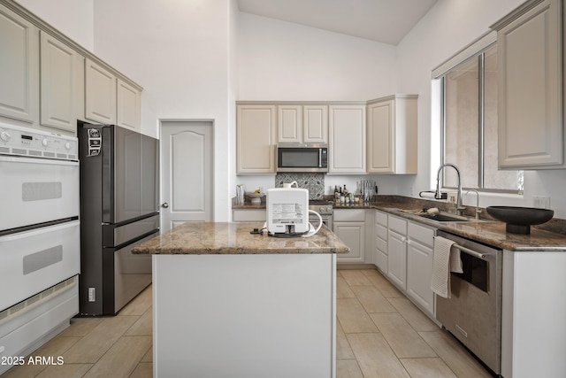 kitchen with dark stone countertops, a kitchen island, sink, appliances with stainless steel finishes, and high vaulted ceiling