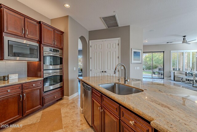 kitchen featuring sink, ceiling fan, stainless steel appliances, light stone countertops, and backsplash