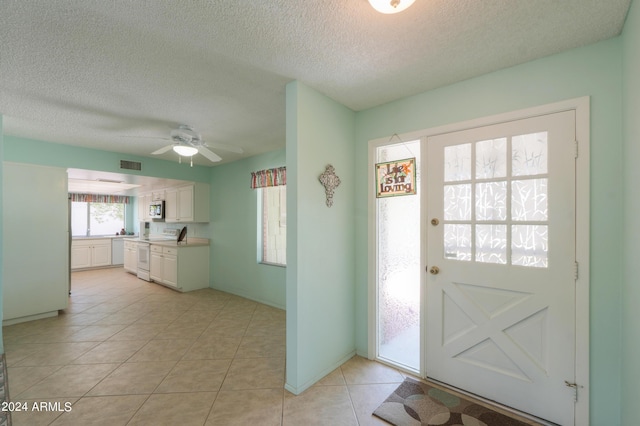 doorway featuring light tile patterned floors, a textured ceiling, visible vents, and a ceiling fan