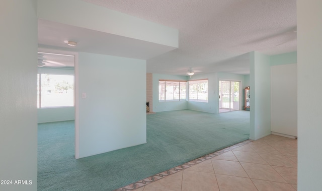 empty room featuring light tile patterned floors, a textured ceiling, light carpet, a fireplace, and a ceiling fan