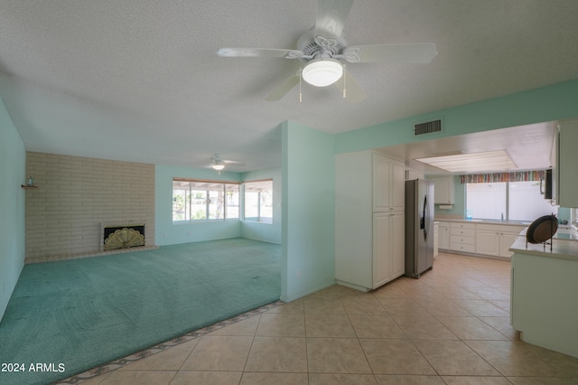 unfurnished living room with ceiling fan, a brick fireplace, a textured ceiling, and light carpet