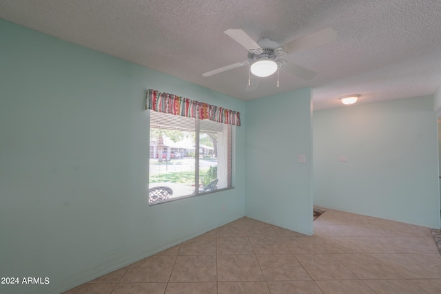 empty room featuring ceiling fan, light tile patterned floors, and a textured ceiling