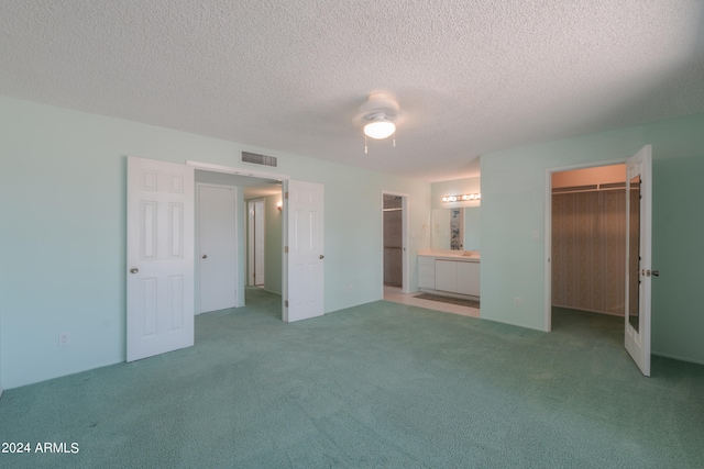 unfurnished bedroom featuring a textured ceiling, ceiling fan, a walk in closet, ensuite bathroom, and carpet