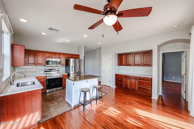 kitchen featuring visible vents, a breakfast bar, a sink, arched walkways, and appliances with stainless steel finishes