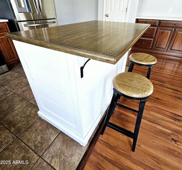 kitchen with a kitchen island, freestanding refrigerator, a kitchen bar, dark countertops, and dark tile patterned floors