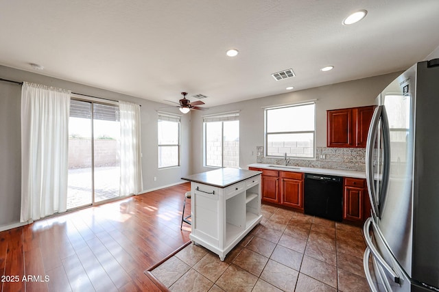 kitchen featuring visible vents, freestanding refrigerator, a sink, black dishwasher, and tasteful backsplash