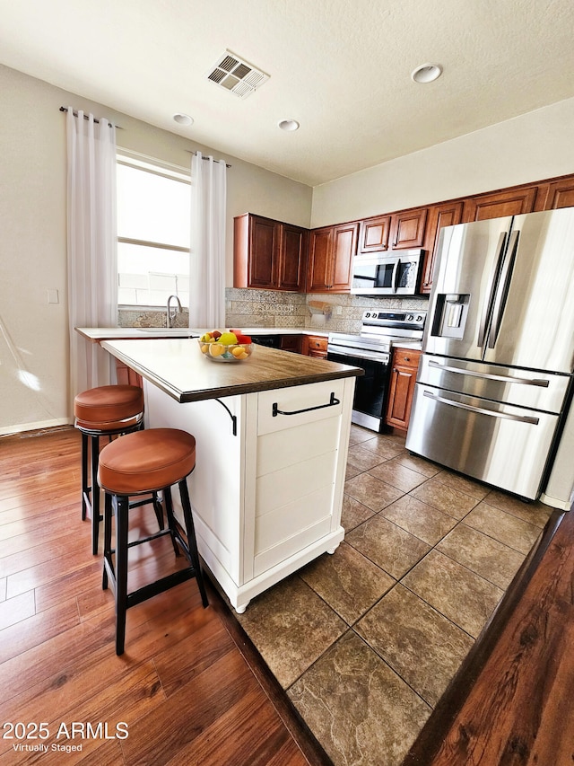 kitchen featuring visible vents, stainless steel appliances, decorative backsplash, a kitchen bar, and a center island