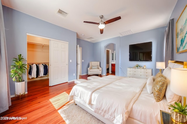 bedroom featuring visible vents, a walk in closet, a closet, wood finished floors, and arched walkways