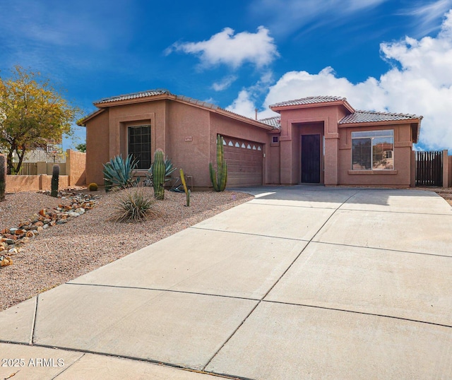 view of front of home with stucco siding, a tile roof, fence, concrete driveway, and a garage