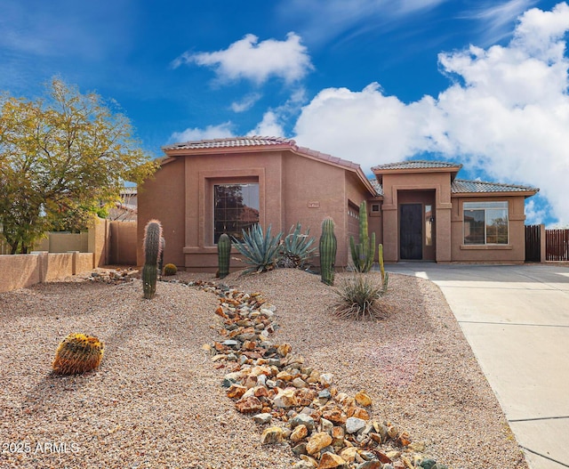 mediterranean / spanish house with a tiled roof, stucco siding, a garage, and fence