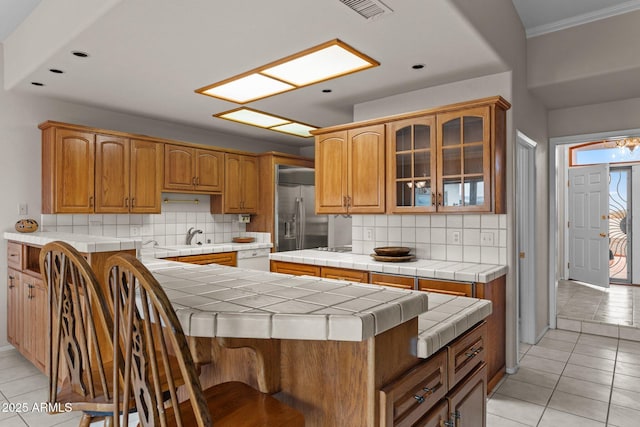 kitchen featuring visible vents, glass insert cabinets, tile counters, stainless steel built in fridge, and light tile patterned floors