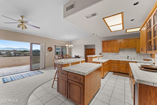 kitchen with visible vents, brown cabinets, glass insert cabinets, light colored carpet, and tile counters