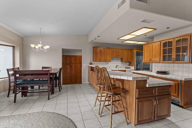 kitchen with backsplash, glass insert cabinets, a kitchen island, and tile counters