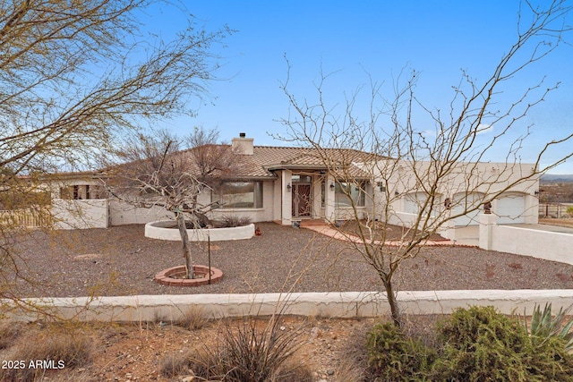 view of front of property with stucco siding, a tiled roof, a chimney, and fence