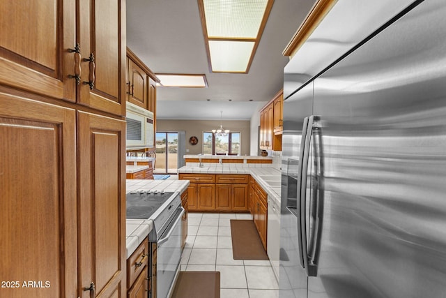 kitchen featuring light tile patterned floors, electric range oven, tile counters, stainless steel fridge, and brown cabinets