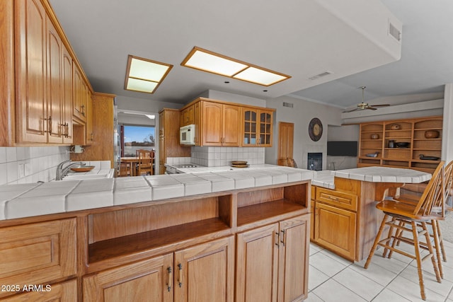 kitchen featuring visible vents, a sink, a peninsula, light tile patterned flooring, and white microwave