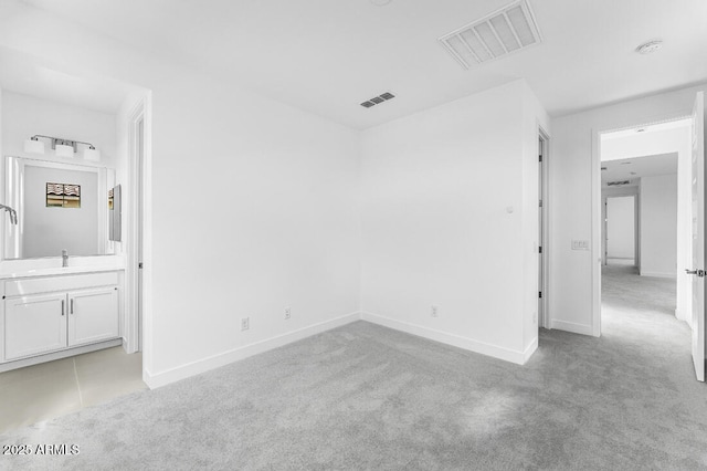 unfurnished bedroom featuring baseboards, visible vents, a sink, and light colored carpet