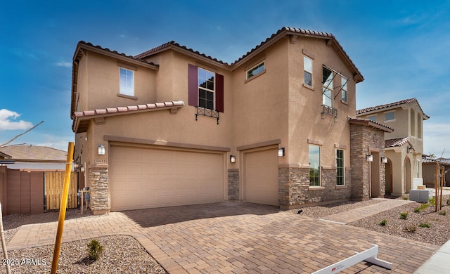 mediterranean / spanish house with stone siding, an attached garage, stucco siding, and decorative driveway