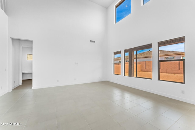 tiled empty room with baseboards, visible vents, a high ceiling, and a healthy amount of sunlight
